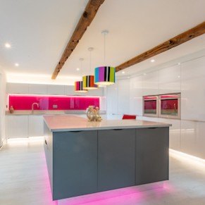 A curved, white kitchen with grey counters and handleless cabinets, lit by purple strip lighting.