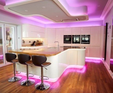 A glossy white kitchen with a curved island breakfast bar and pink strip lighting.