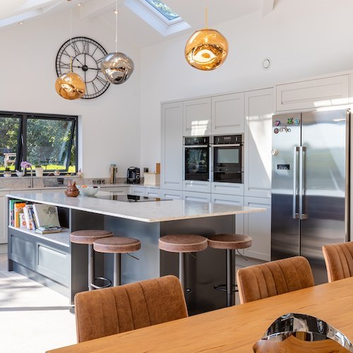 A modern white kitchen with a long dining table and upholstered chairs.