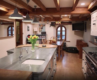 A country style kitchen with a curved grey and wood island and exposed wood beam ceiling.