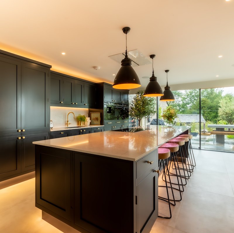 A grey and blue kitchen with a marble island with glass drop shape lights.